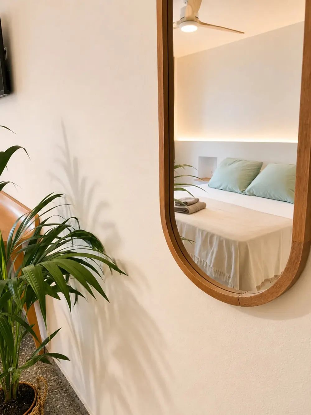 Espejo ovalado con marco de madera y una planta en una habitación del Hotel S'Algaret